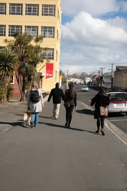 Four people and a dog walking down the street.