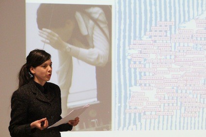 A woman giving a presentation while hold a stack of paper.