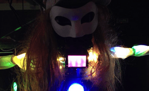 A masked figure with long hair, covered in lights.