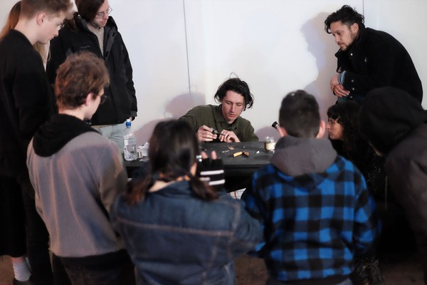 A group of people watching a man at a desk.