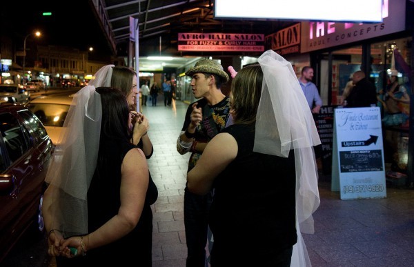 A man in a hat talking with three woman wearing bridal veils.