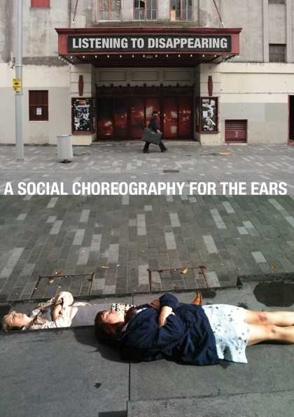 Two people lying in the gutter of a street, their arms cross across their chests.